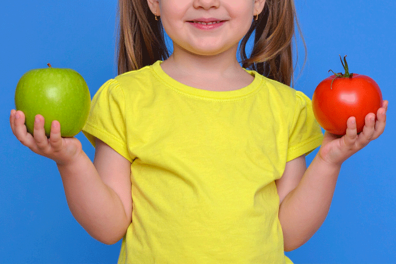 pädagogische-akademie-praxisideen10 Pädagogische Akademie, Praxisideen, Kilos in der Waagschale, Mädchen hält einen grünen Apfel und eine rote Tomaten in den Händen